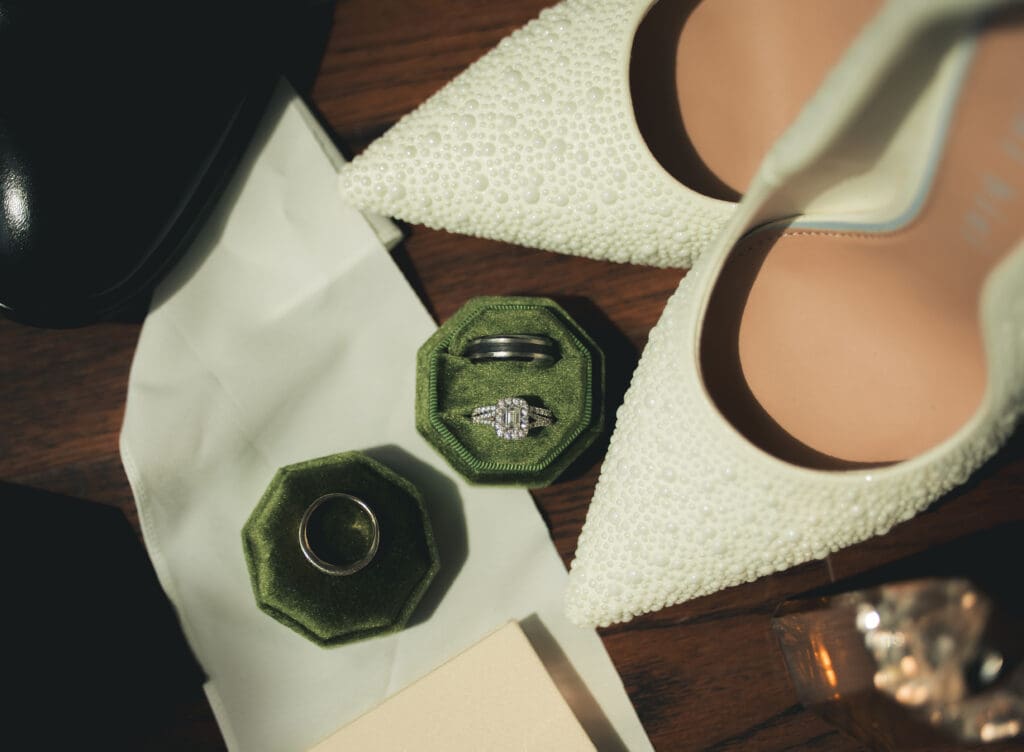 Detail Photos of shoes, a diamond ring, and a mens ring. This image shows the details of a wedding day in a flat lay.